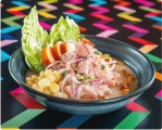Traditional Peruvian cebiche with fish, corn, sweet potato, and red onions in a dark bowl on a colorful table.